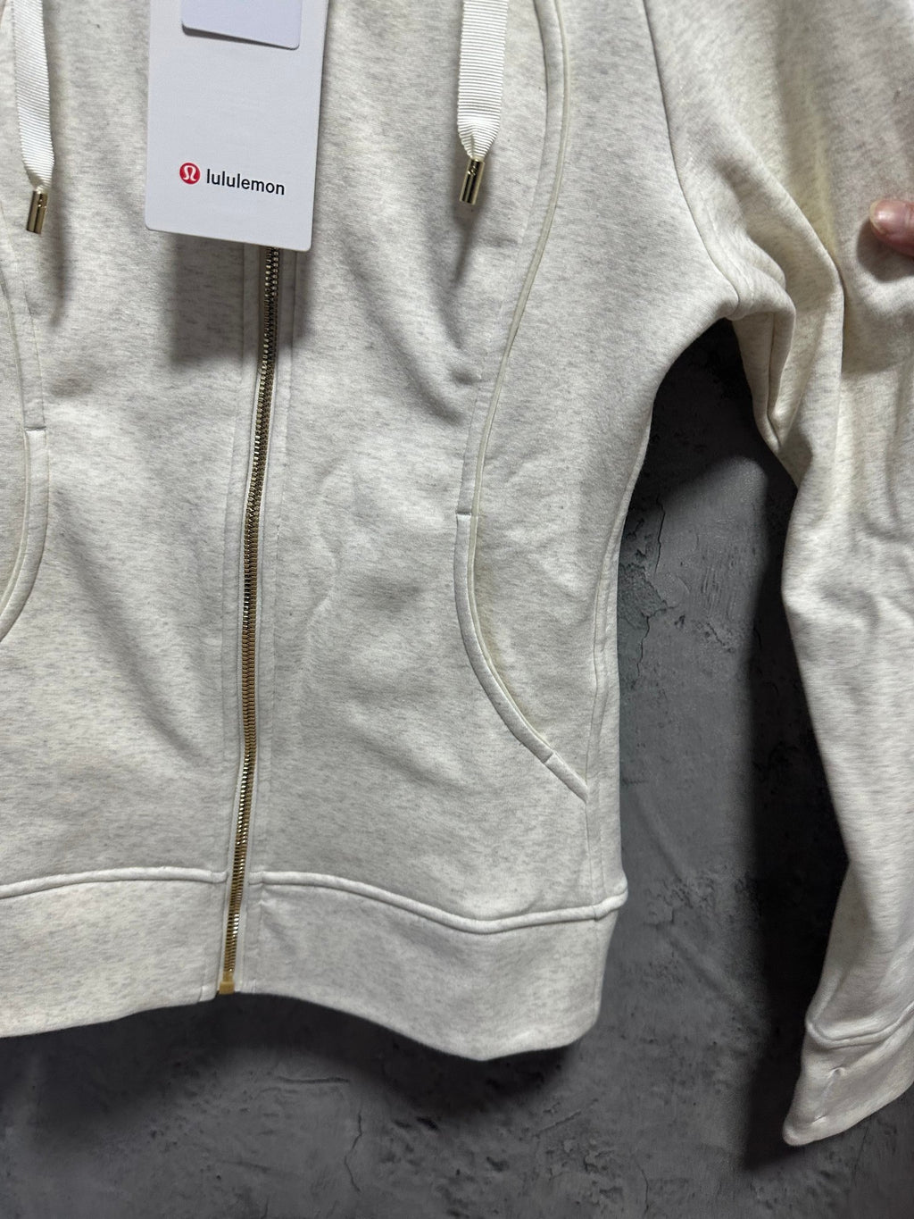 Light cream zip-up hoodie front with gold zipper, hood ties, and kangaroo pocket hem