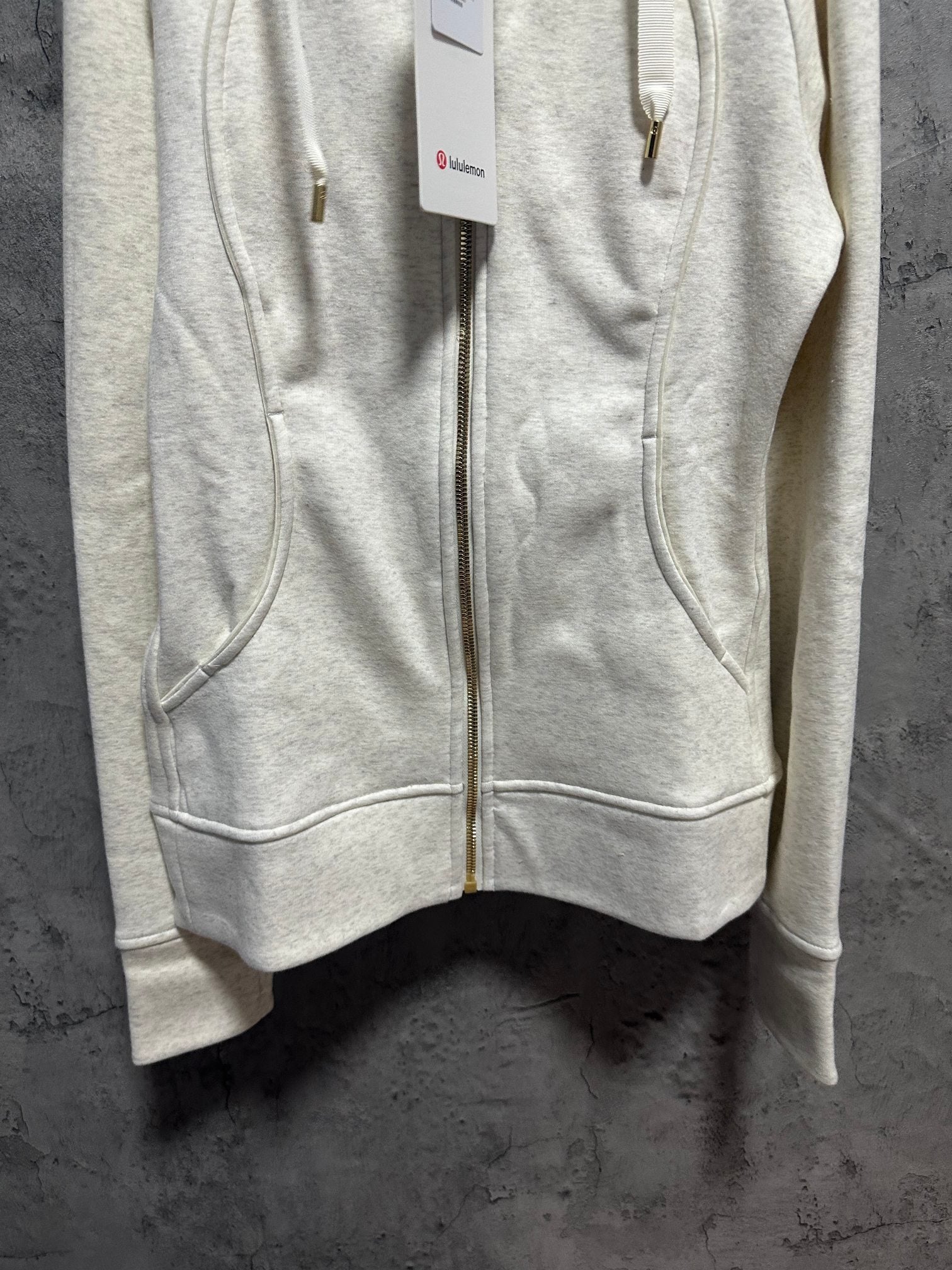 Light cream zip-up hoodie with hood, drawstring ties, and front pockets closed with zipper