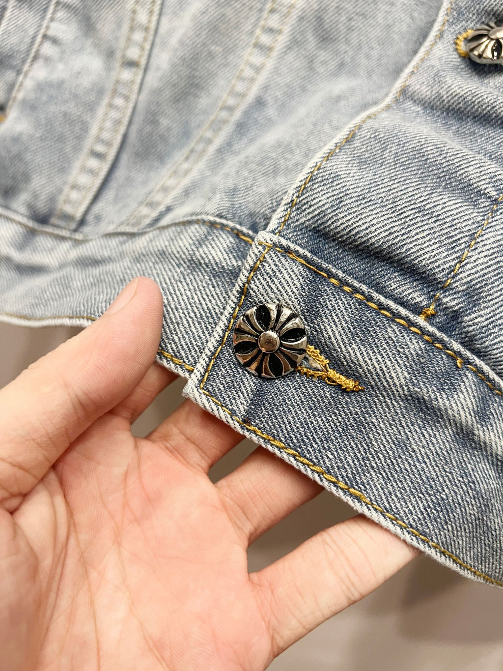 Light-wash denim jacket cuff with small gold button and embroidered flower patch