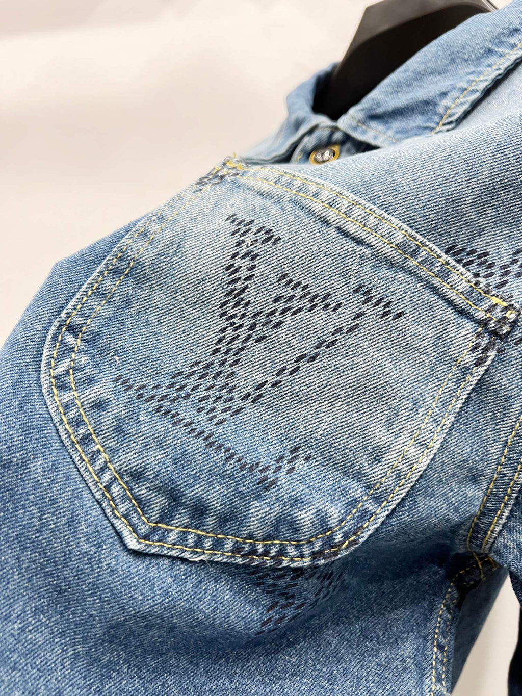 Light blue denim jacket sleeve with monogram design and contrast-stitched seams