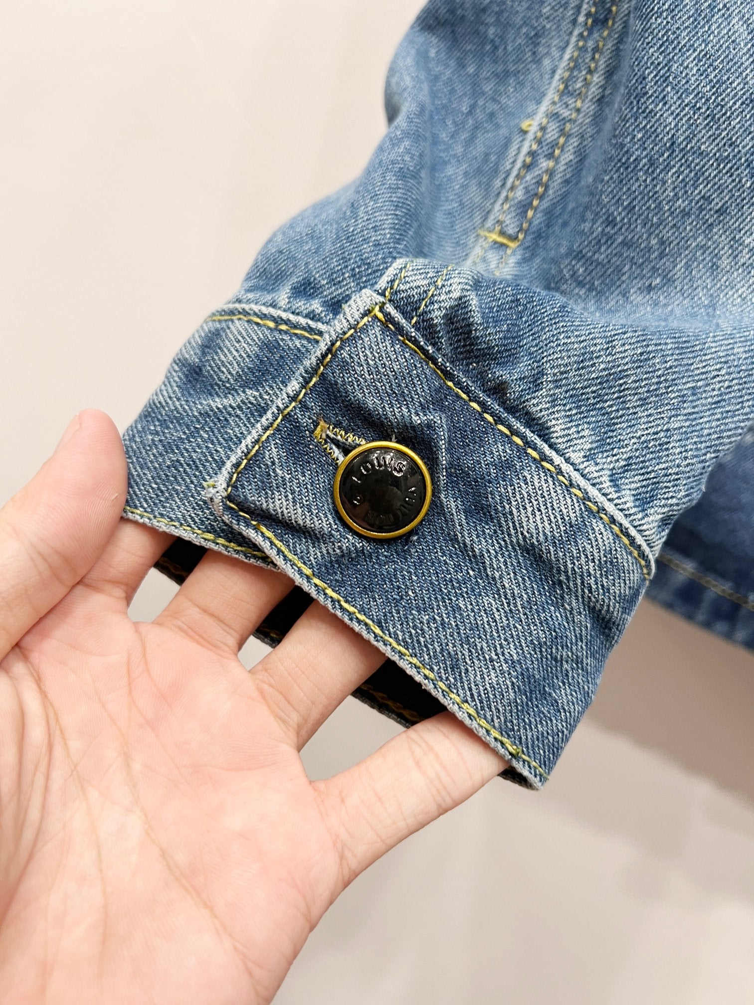 Light blue denim jacket cuff with gold-tone button and contrast stitch trim
