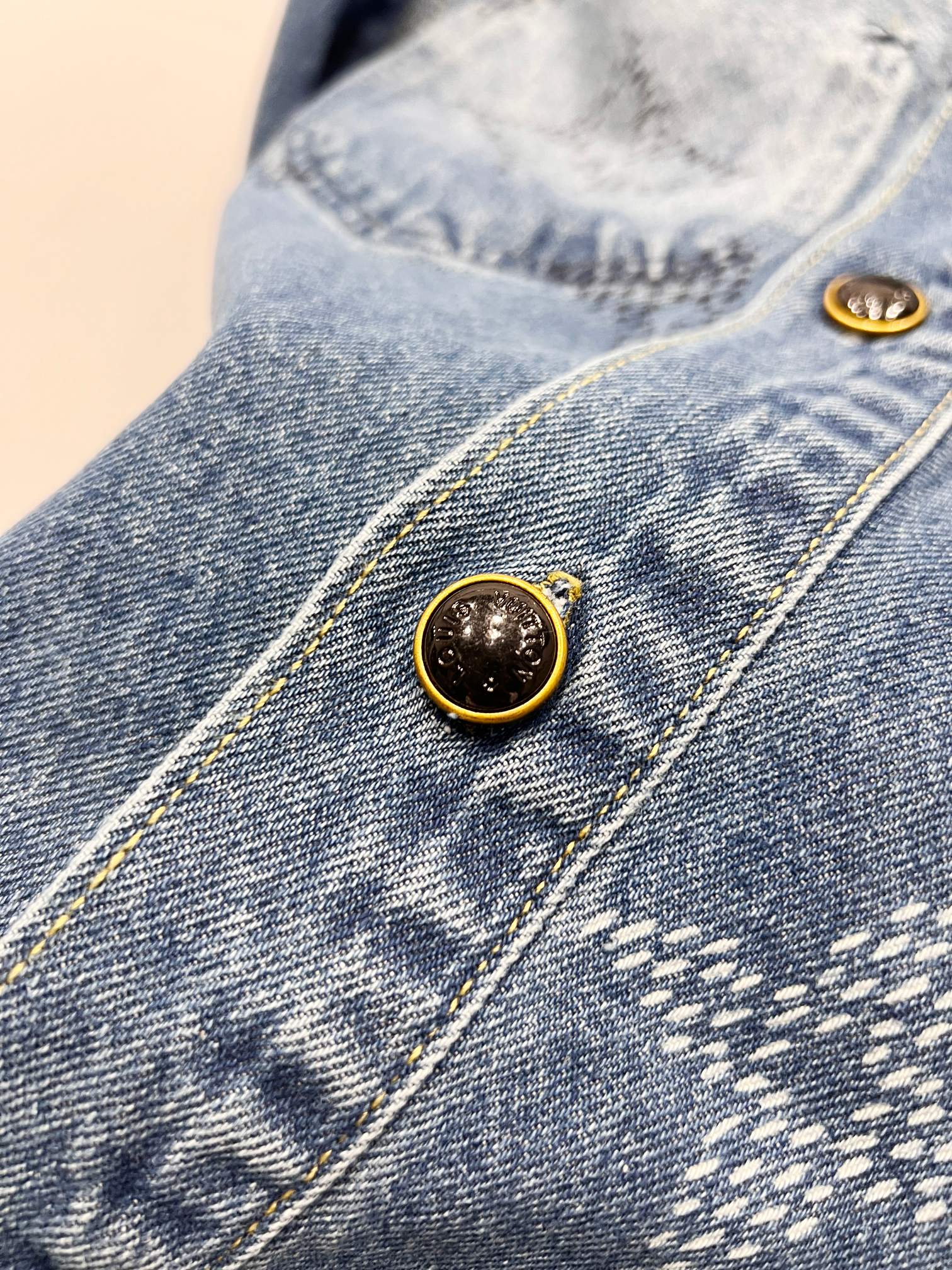 Light blue denim jacket button placket detail with gold-tone round buttons