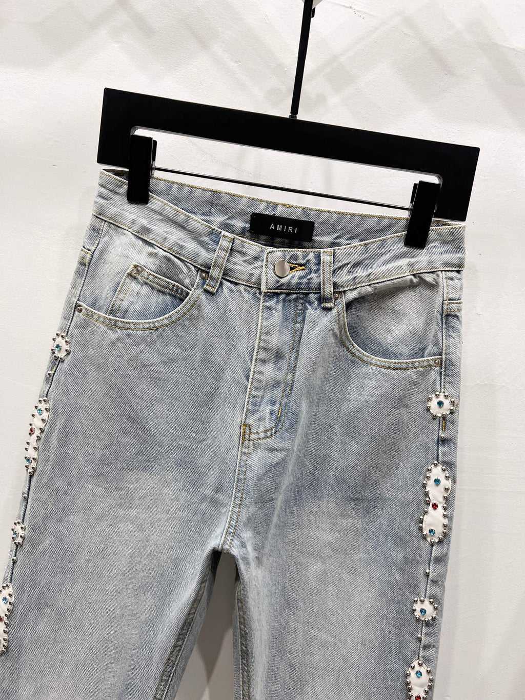 Light blue denim jeans with button fly, front pockets, and jeweled side trim