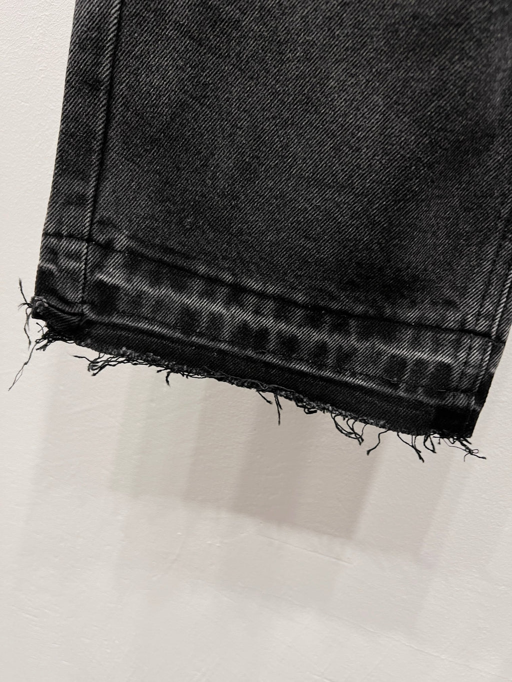 Black denim jeans with frayed raw hem at the cuff