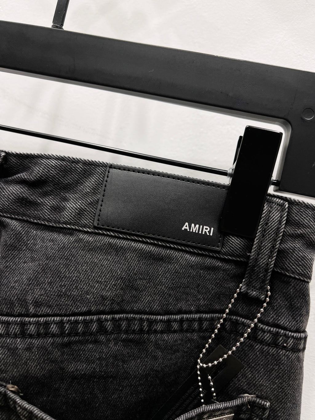 Black denim jeans with front logo patch and chain detail near the pocket