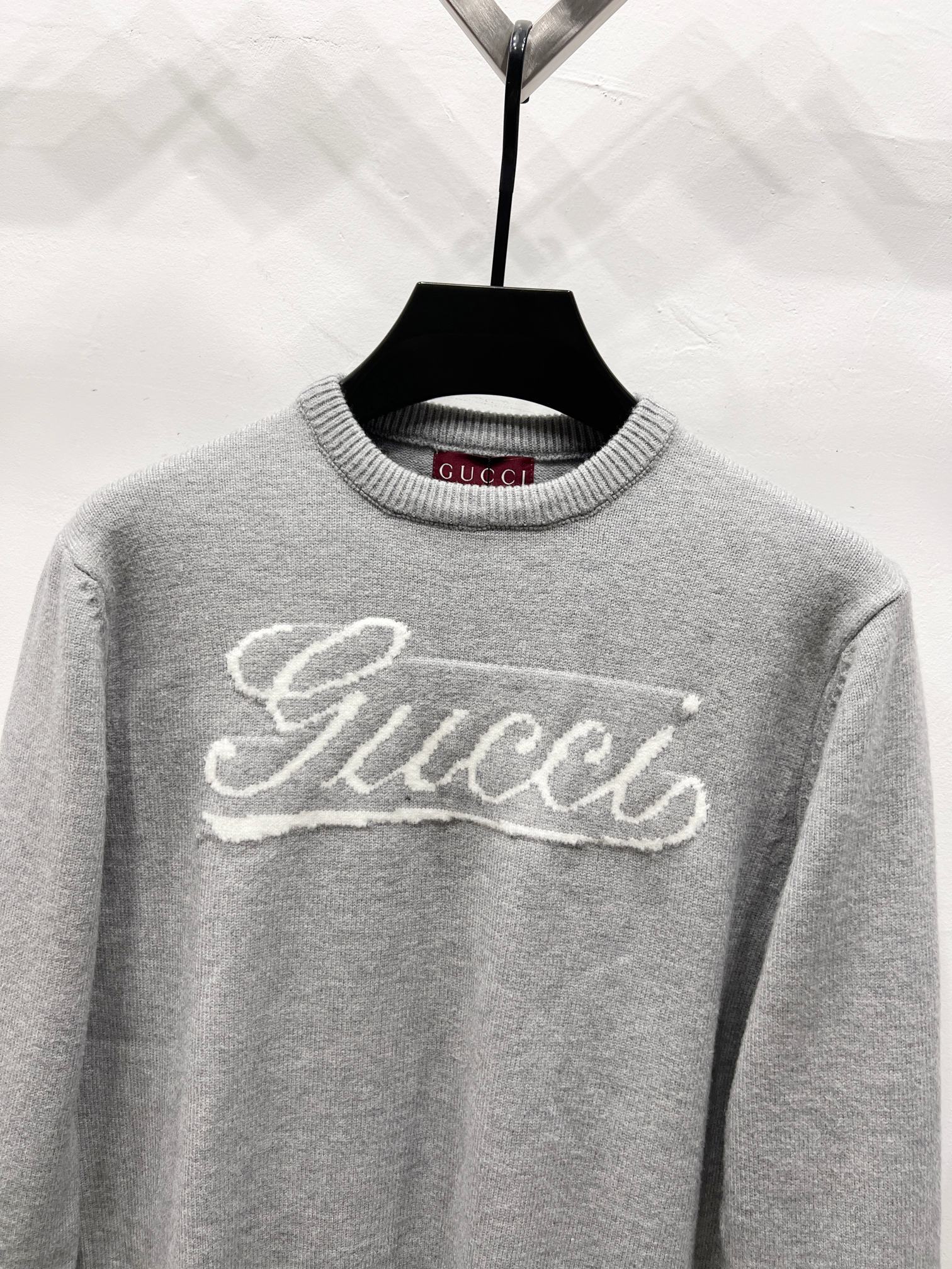 Gray knit sweater with white Gucci script logo across the chest