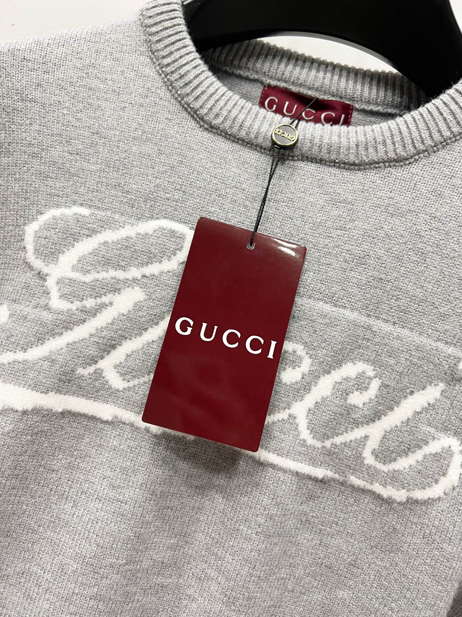 Gray sweater collar with white Gucci logo and hanging red Gucci tag
