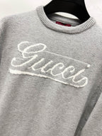 Gray knit sweater with white Gucci script logo across the front