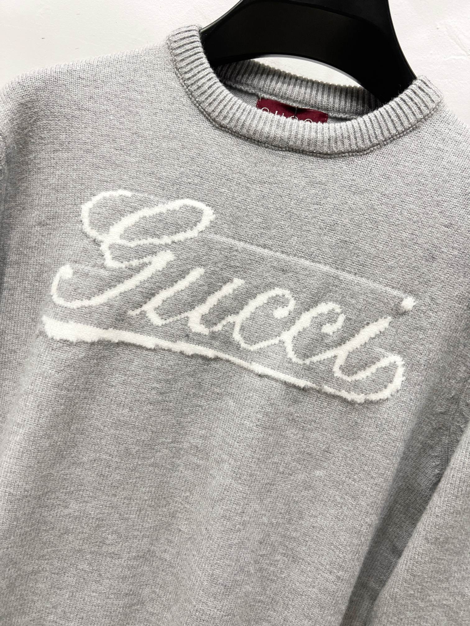 Gray knit sweater with white Gucci script logo across the front