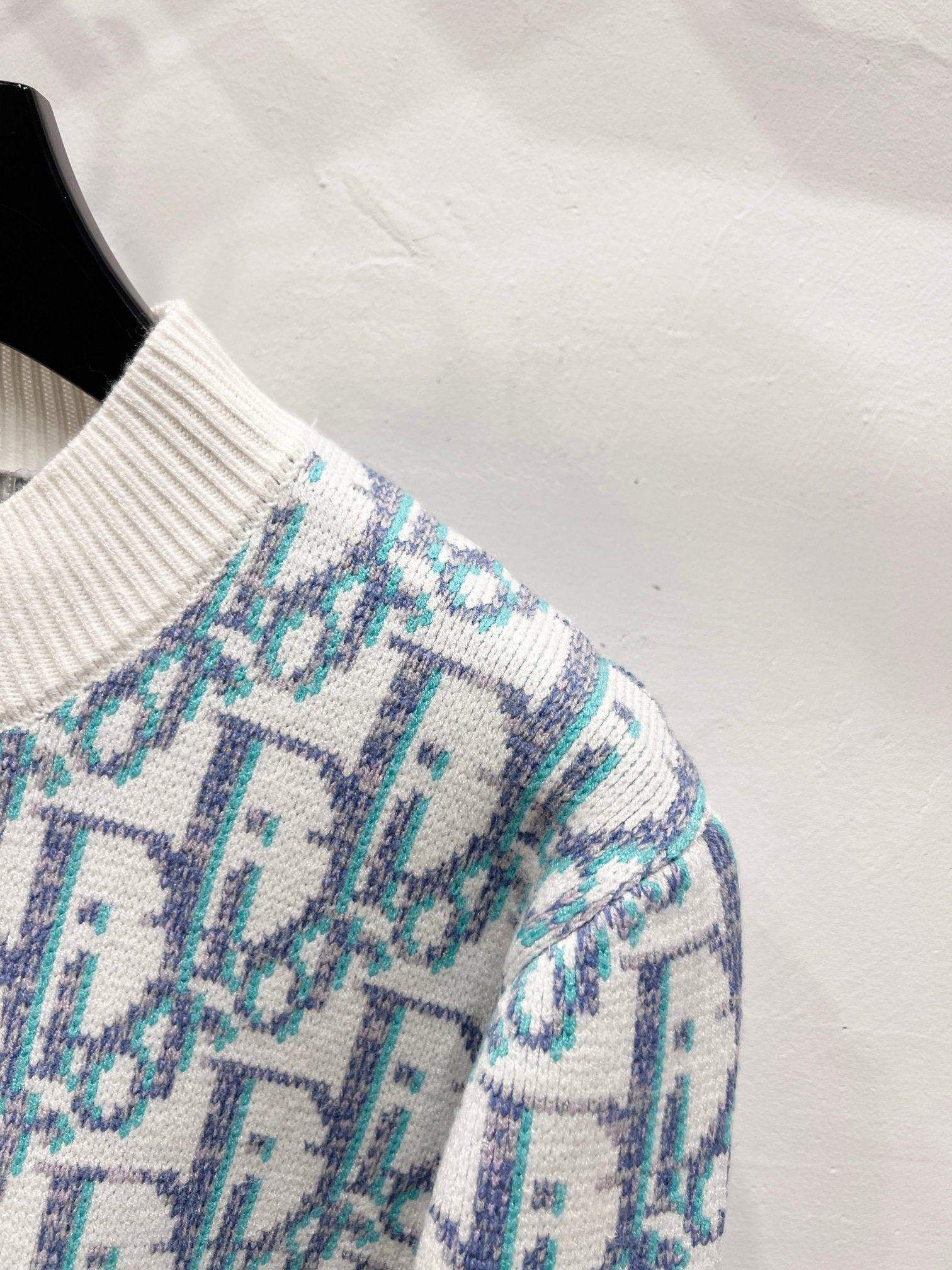 Knitted sleeve cuff and shoulder, light blue logo pattern on off-white ribbed trim