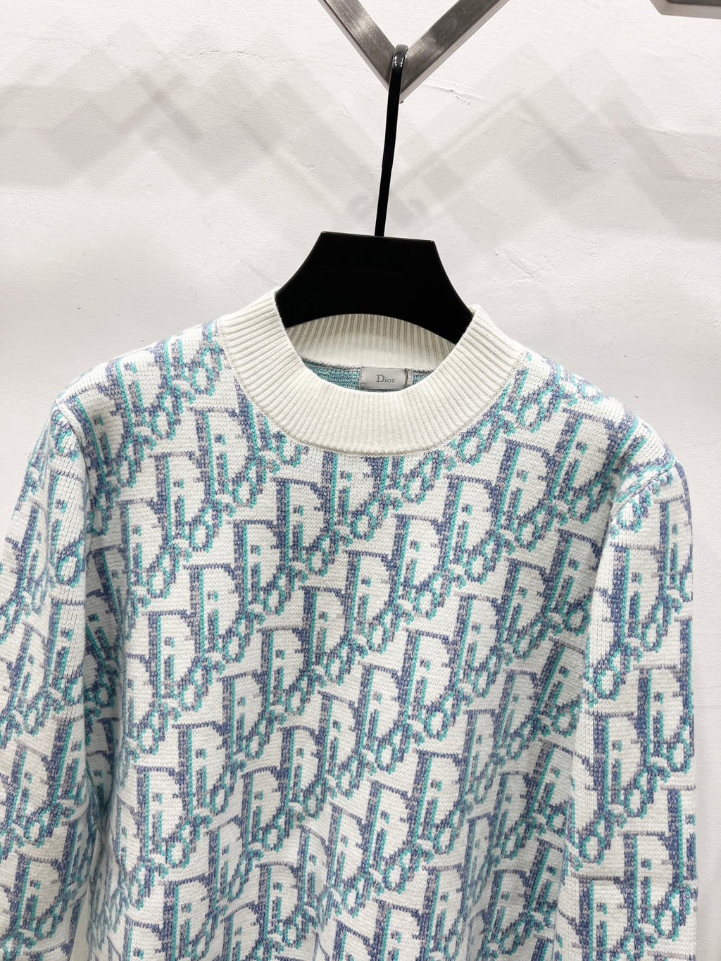 Crew-neck knit sweater close-up, light blue and teal logo pattern on off-white