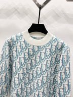 Crew-neck knit sweater close-up, light blue and teal logo pattern on off-white