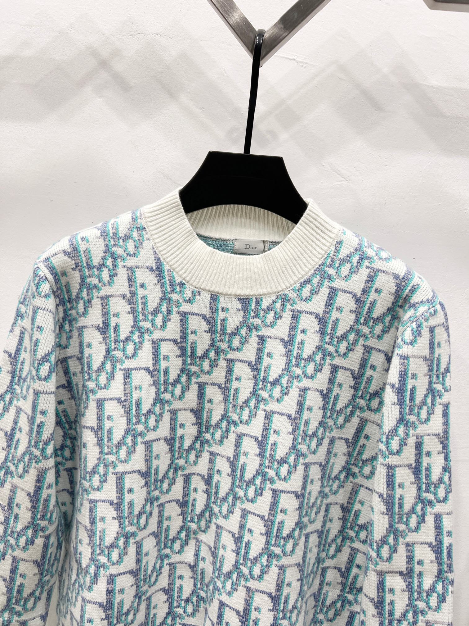Crew-neck knit sweater close-up, light blue and teal logo pattern on off-white