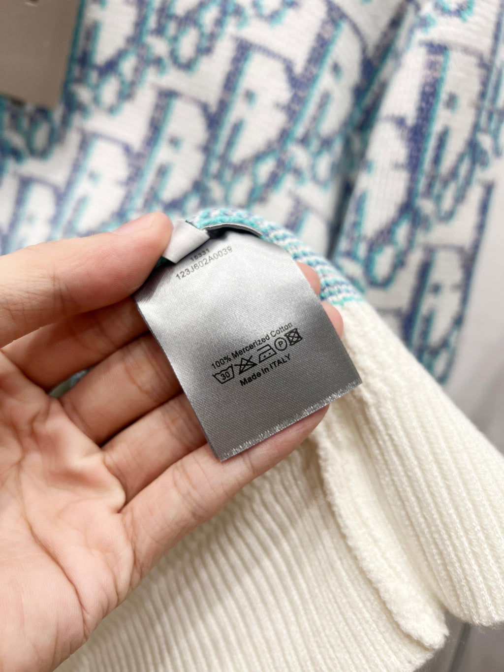 Care label inside neck on sweater, off-white knit with light blue logo pattern