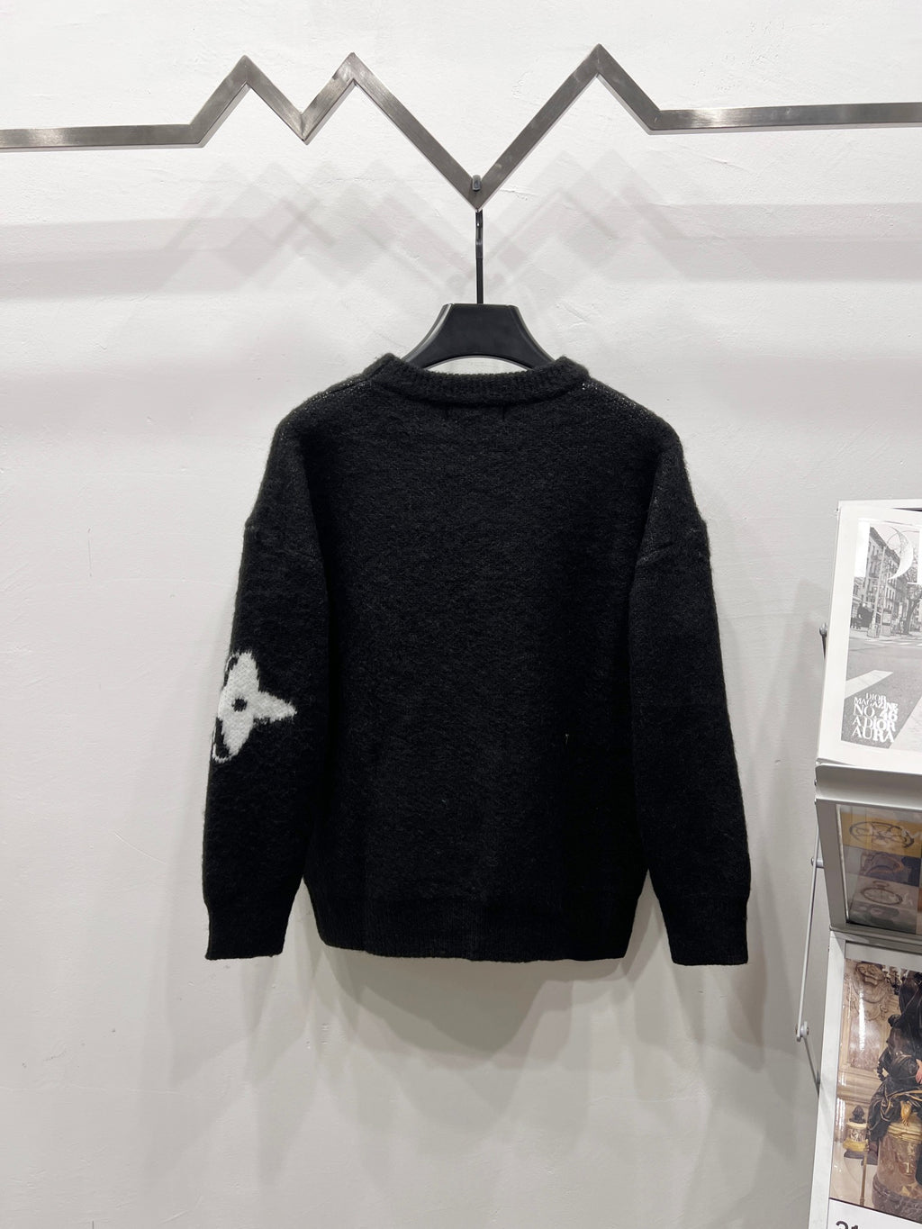 Black crewneck knit sweater back with partial white graphic on left sleeve