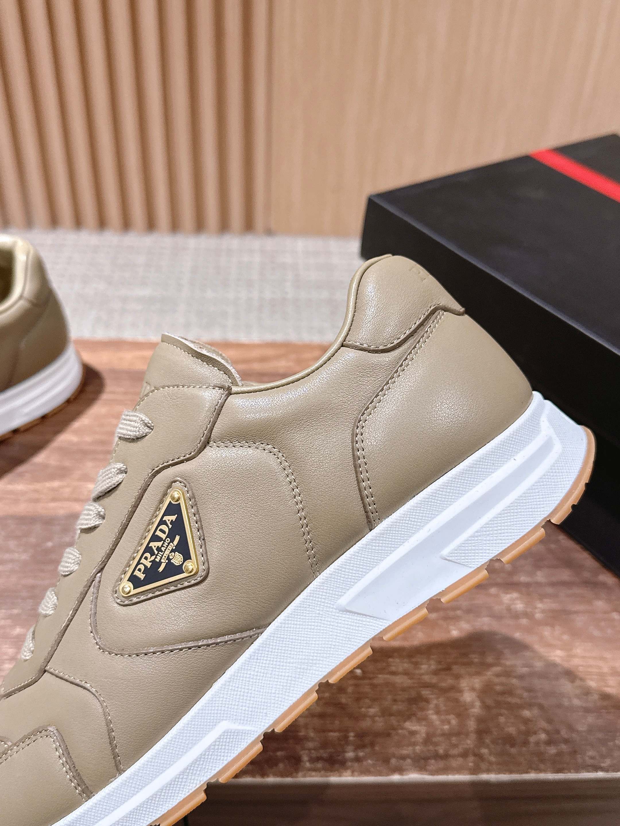 Prada unisex light beige sneaker with lace-up front and triangular logo patch.