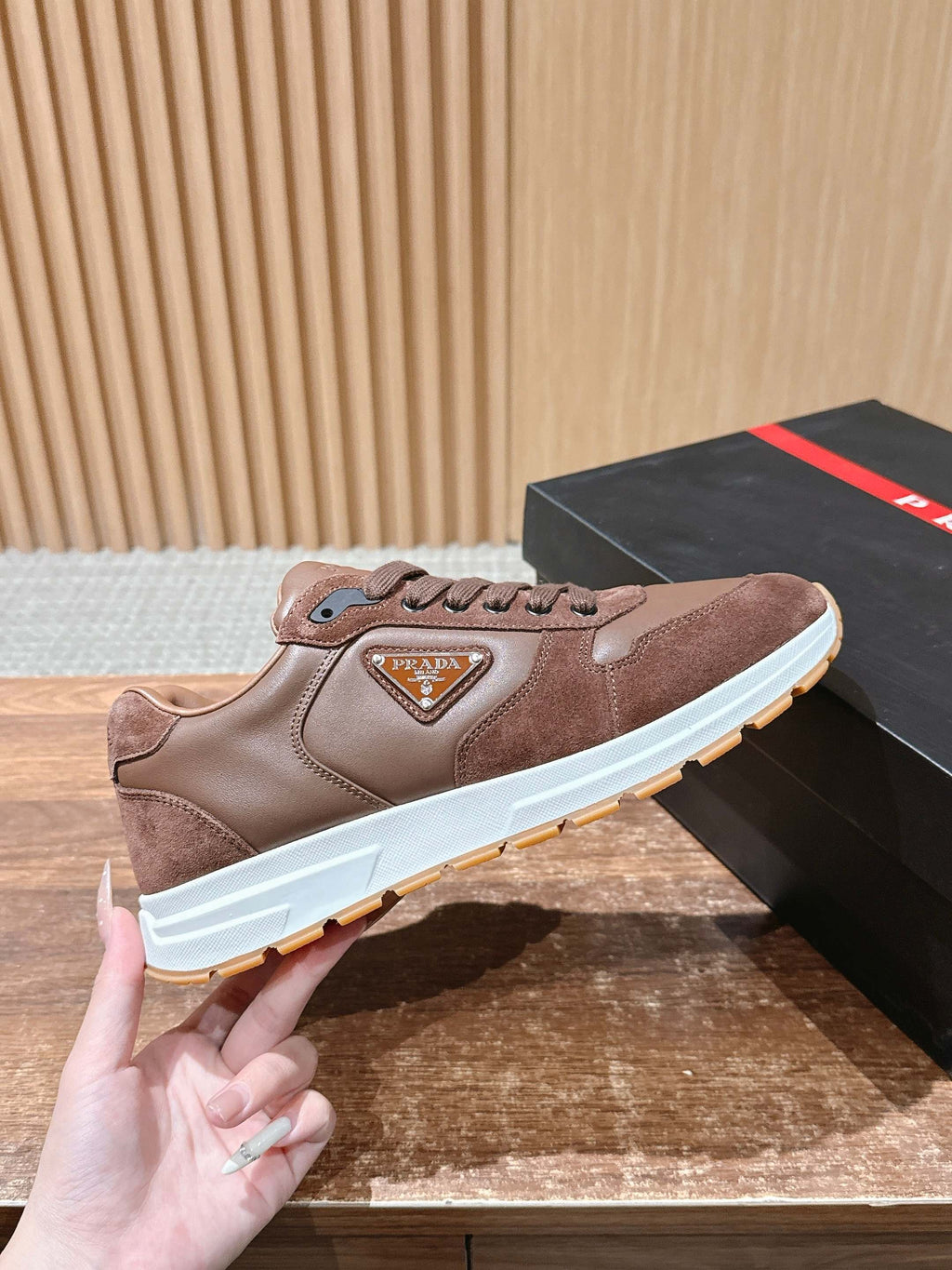 Taupe leather sneaker with lace-up closure and triangular logo badge.