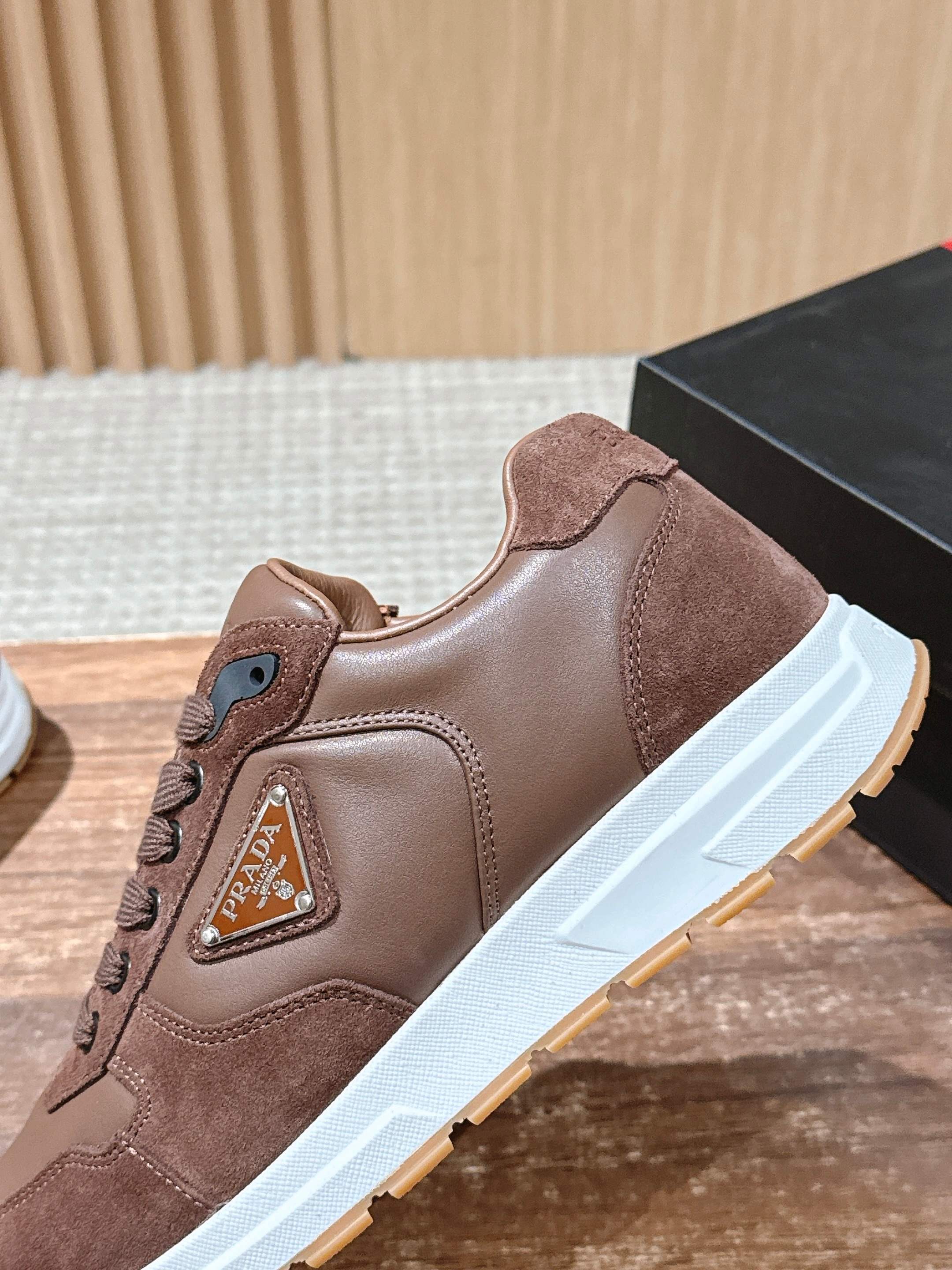Taupe leather sneaker with lace-up, logo badge, and white sole.