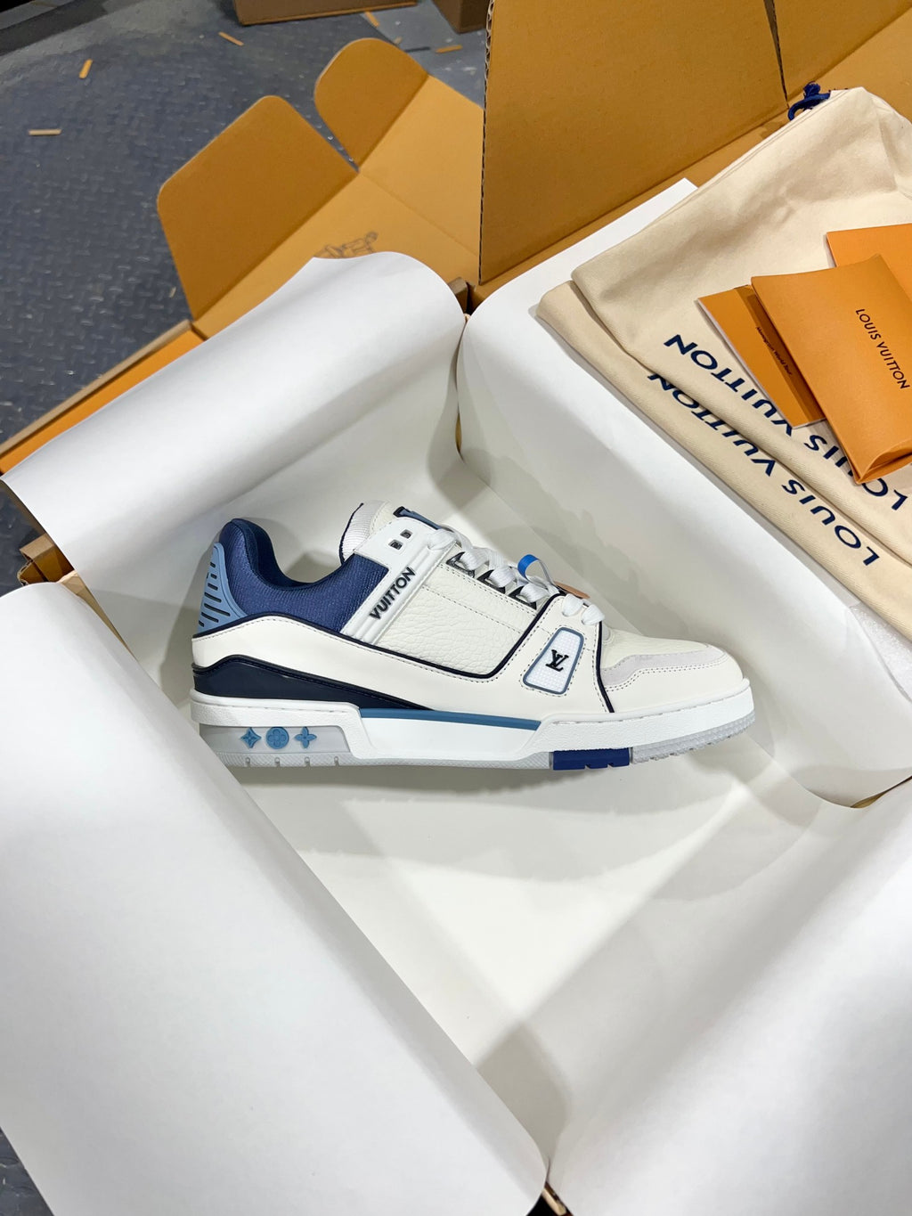 Louis Vuitton trainer sneakers, side view in white with navy trim and LV logo on strap.