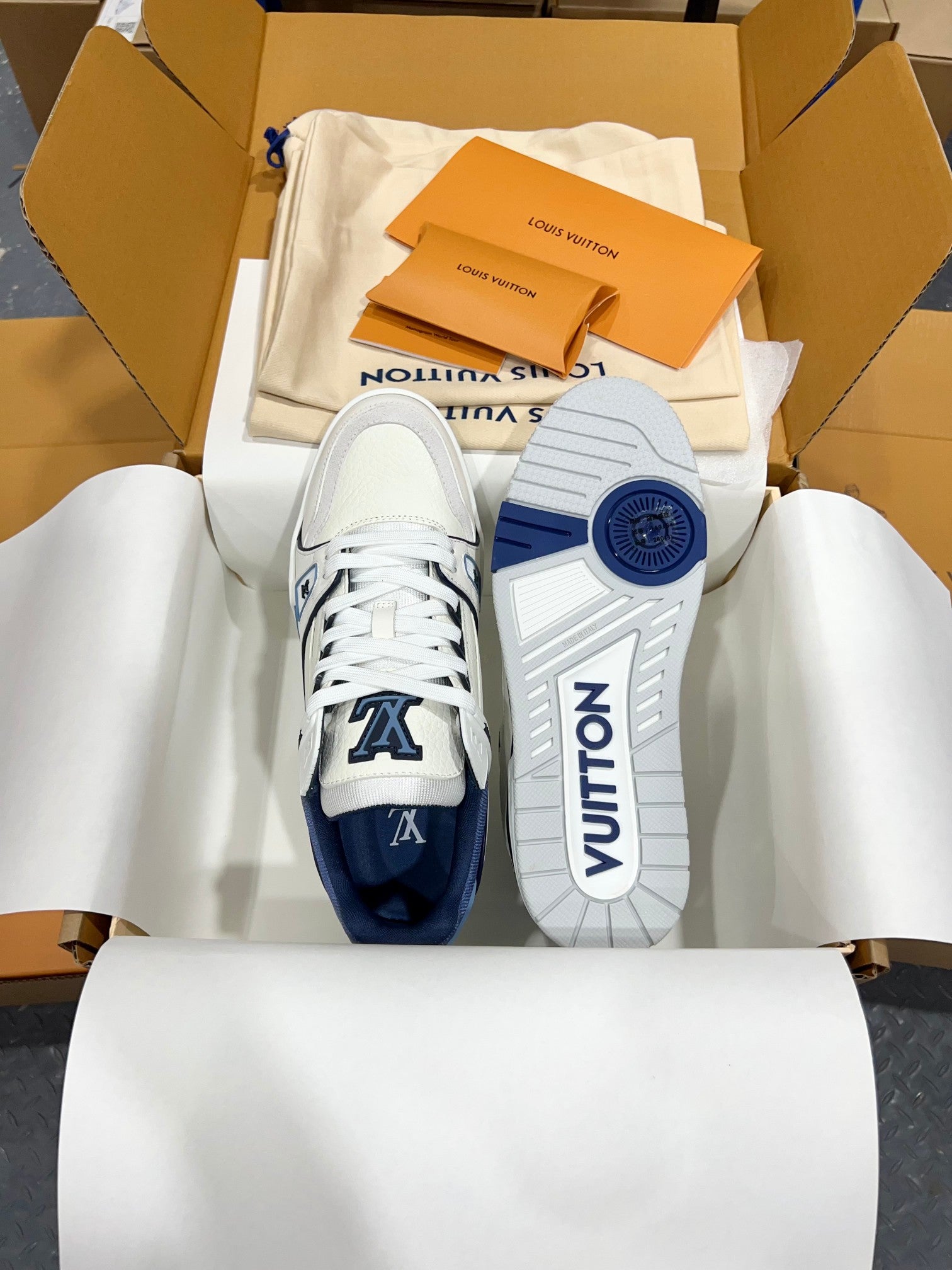 Louis Vuitton trainer sneakers, front view with white laces, navy toe caps, and LV branding.