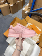 Louis Vuitton pink low-top sneakers with white laces, held above an open shoebox.