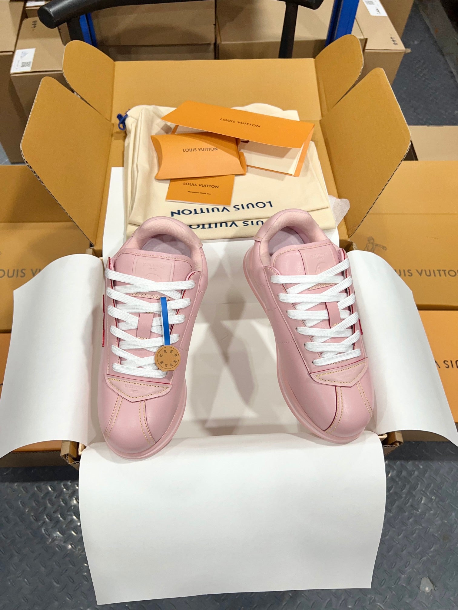 Louis Vuitton pink low-top sneakers with white laces, front view in open shoebox.