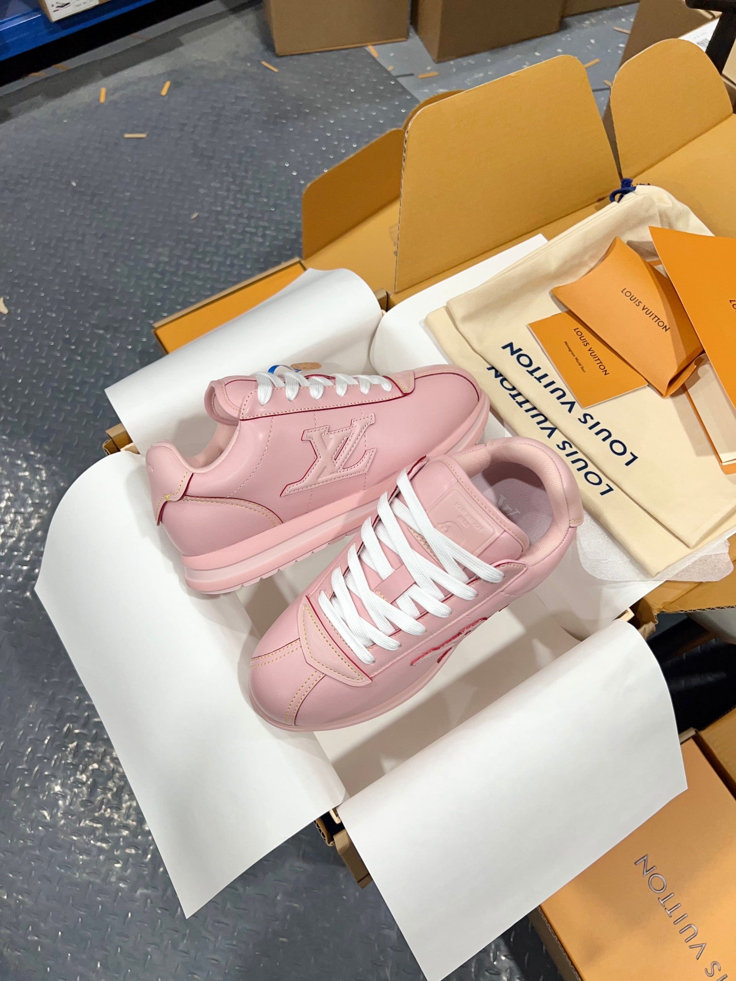 Louis Vuitton pink low-top sneakers with white laces, side view with LV-style logo on box.