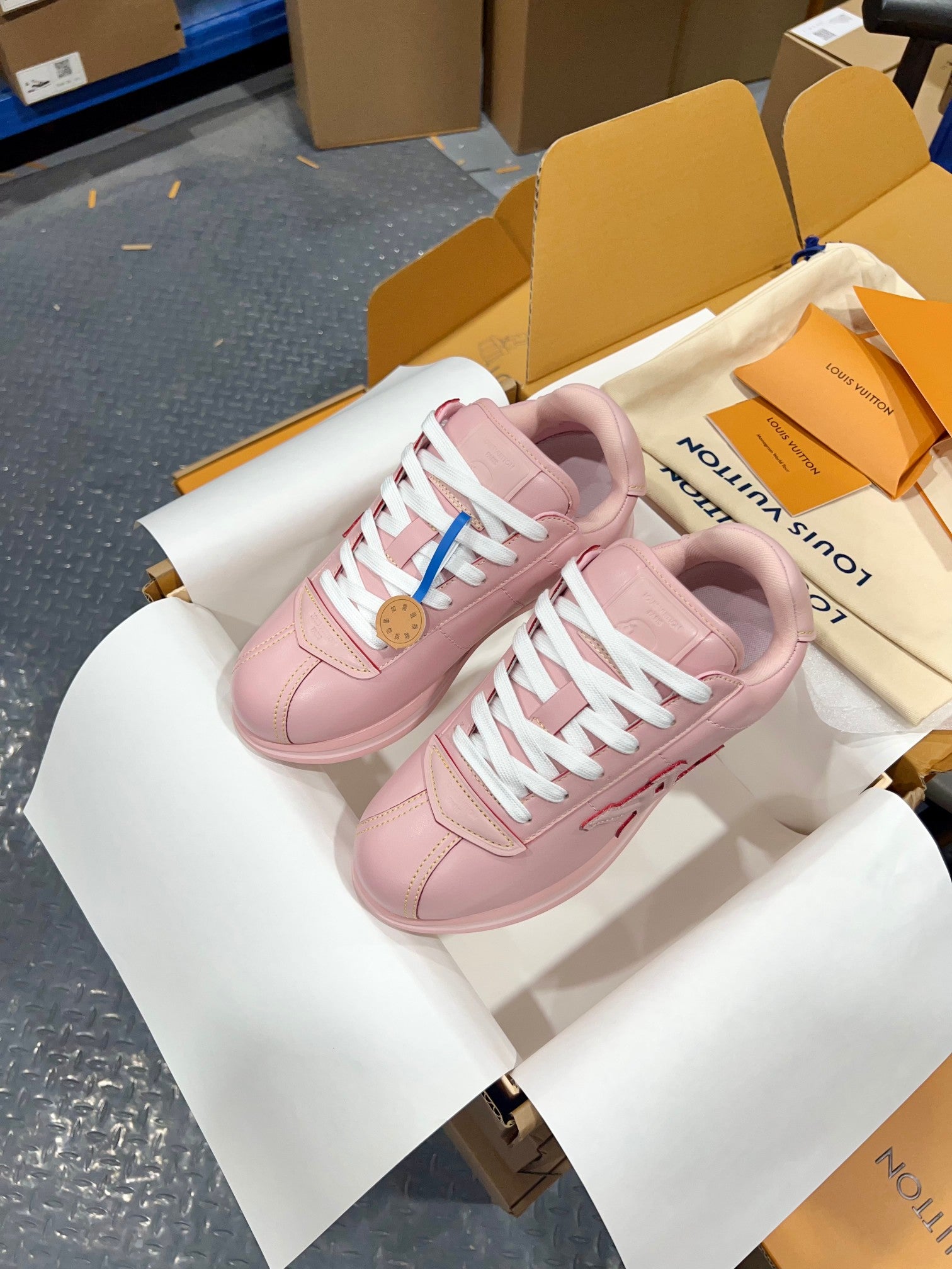Louis Vuitton pink low-top sneakers with white laces, side view on a white shoebox insert.