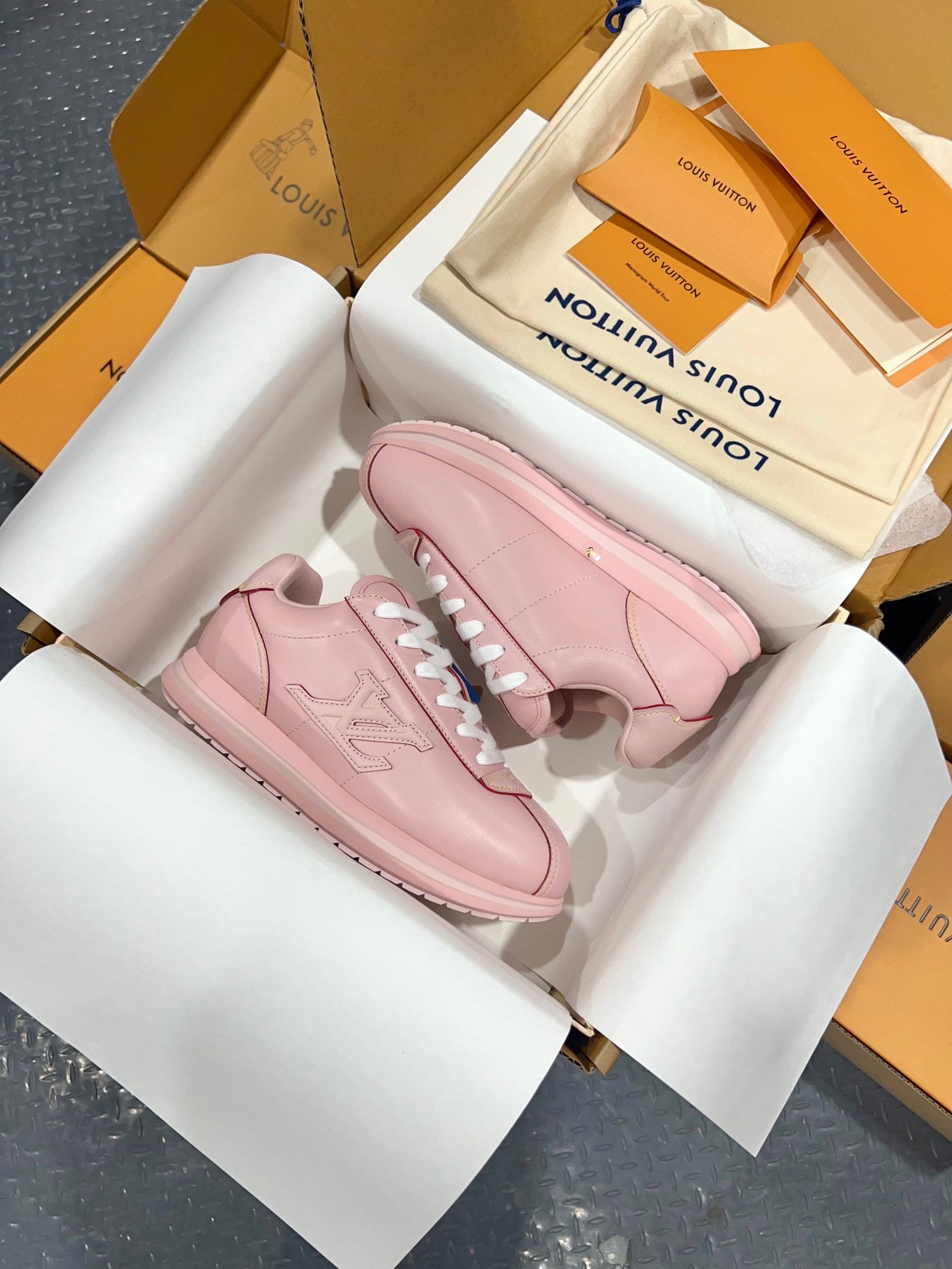 Louis Vuitton pink low-top sneakers with white laces, angled view inside open shoebox.