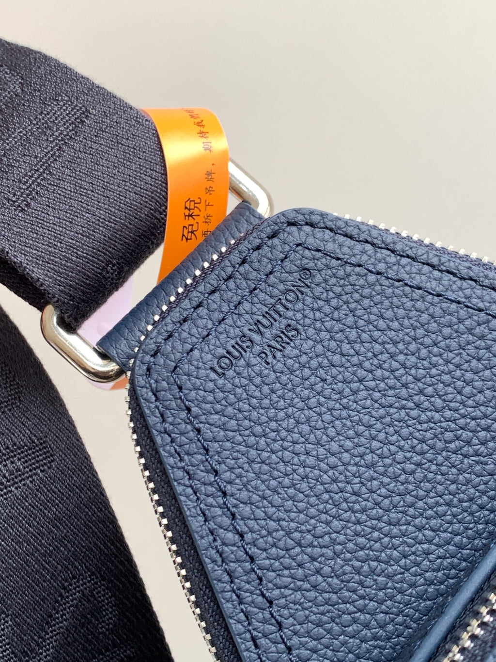 Dark blue pebble-grain leather bag with zipper edge and embossed logo text