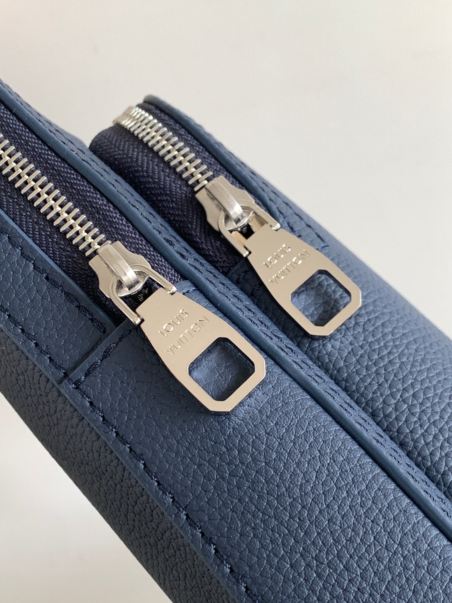 Zipper track on dark blue leather bag, gold-tone dual sliders with pull tabs