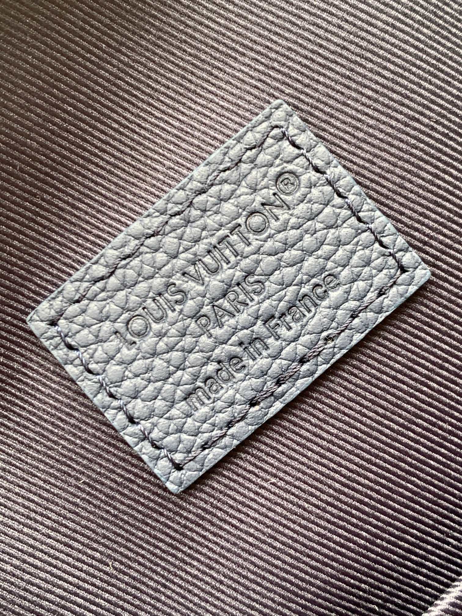 Embossed leather logo patch on bag, Louis Vuitton text on light gray panel