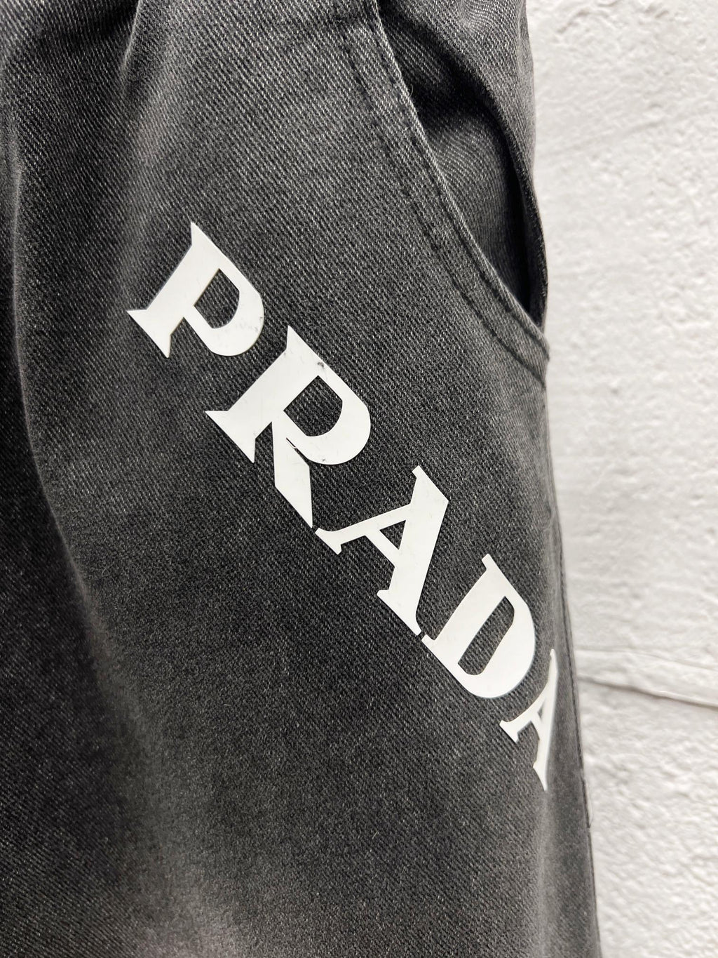Gray denim pants side close-up with white PRADA lettering