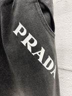 Close-up of dark gray denim pants with large white PRADA lettering