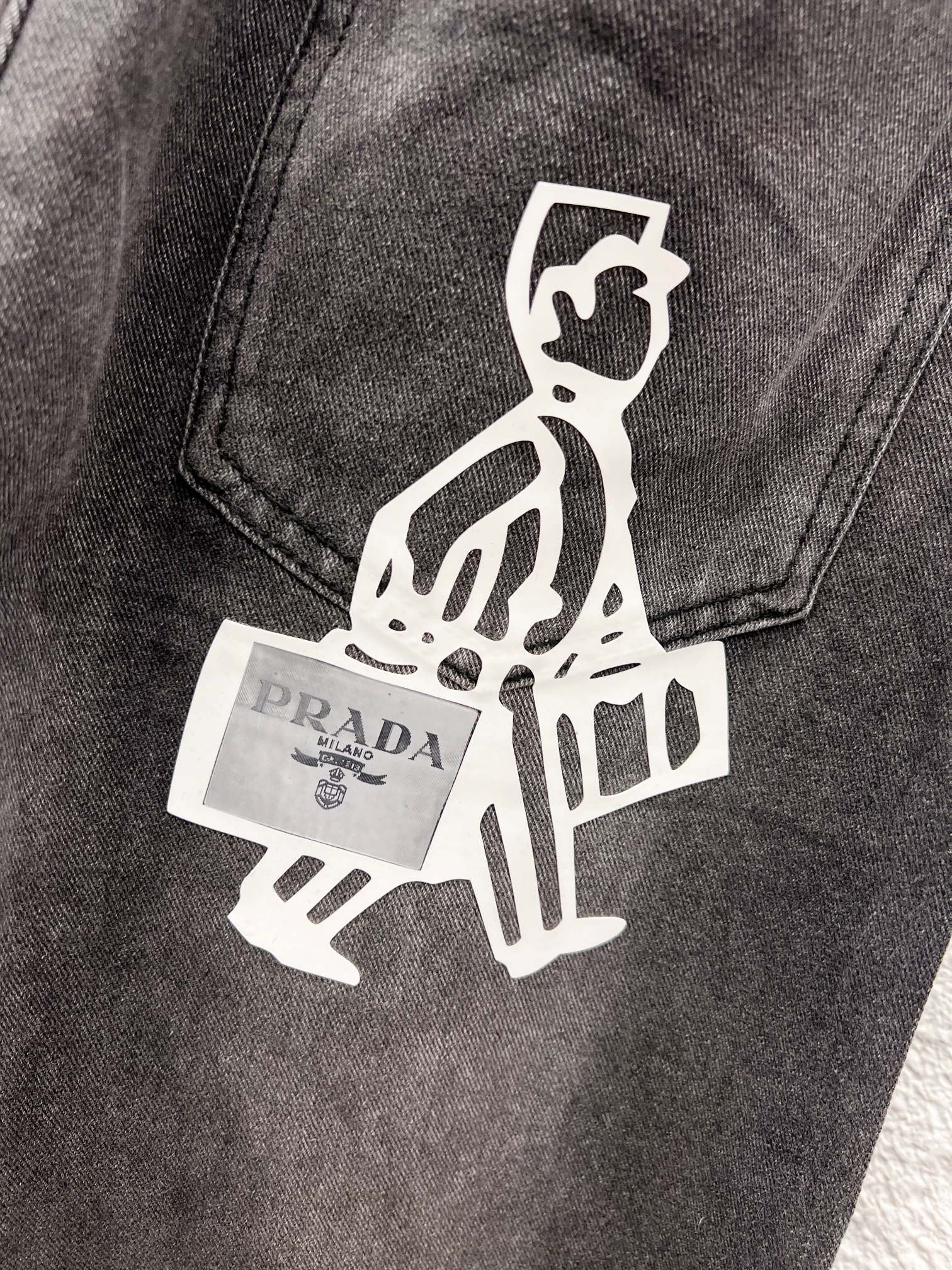 Gray denim pants close-up of white logo graphic with small Prada label