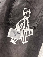 Close-up of dark gray denim pants with white graphic patch and PRADA label