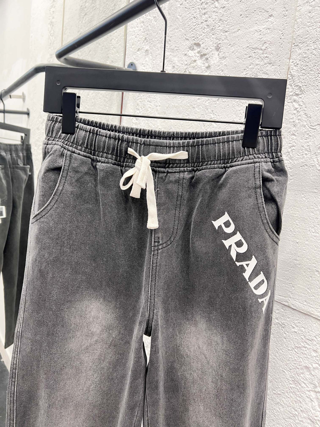 Dark gray denim pants with drawstring waist and PRADA lettering on thigh