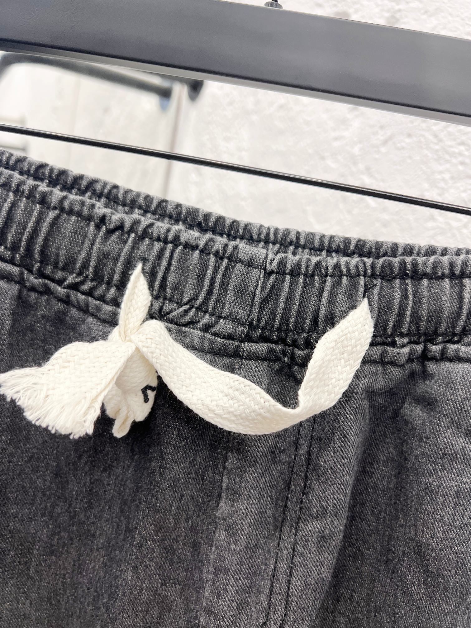 Dark gray denim pants waistband with white drawstring bow detail