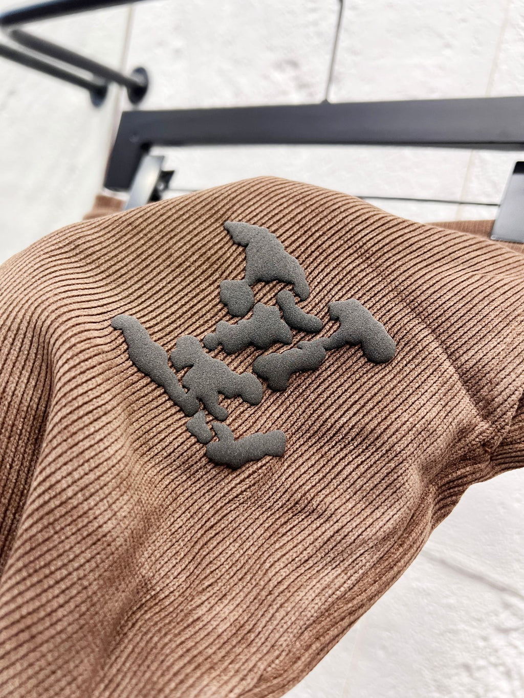 Brown corduroy pants with dark embroidered logo patch on the leg