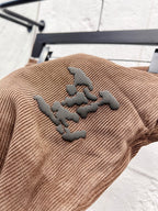 Brown corduroy pants with dark embroidered logo patch on the leg