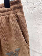 Brown corduroy pants side view with drawstring and embroidered logo detail