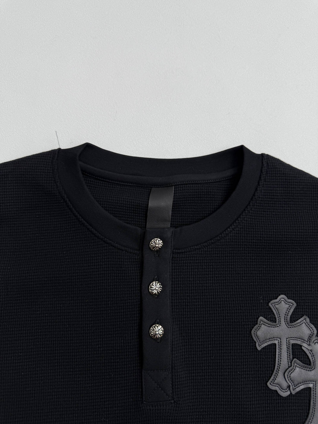 Black long-sleeve henley neckline with three button placket and textured panel detail