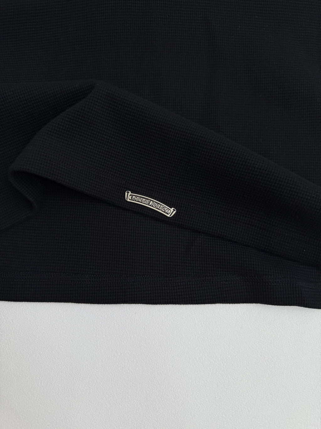 Black long-sleeve shirt cuff label detail on the sleeve hem