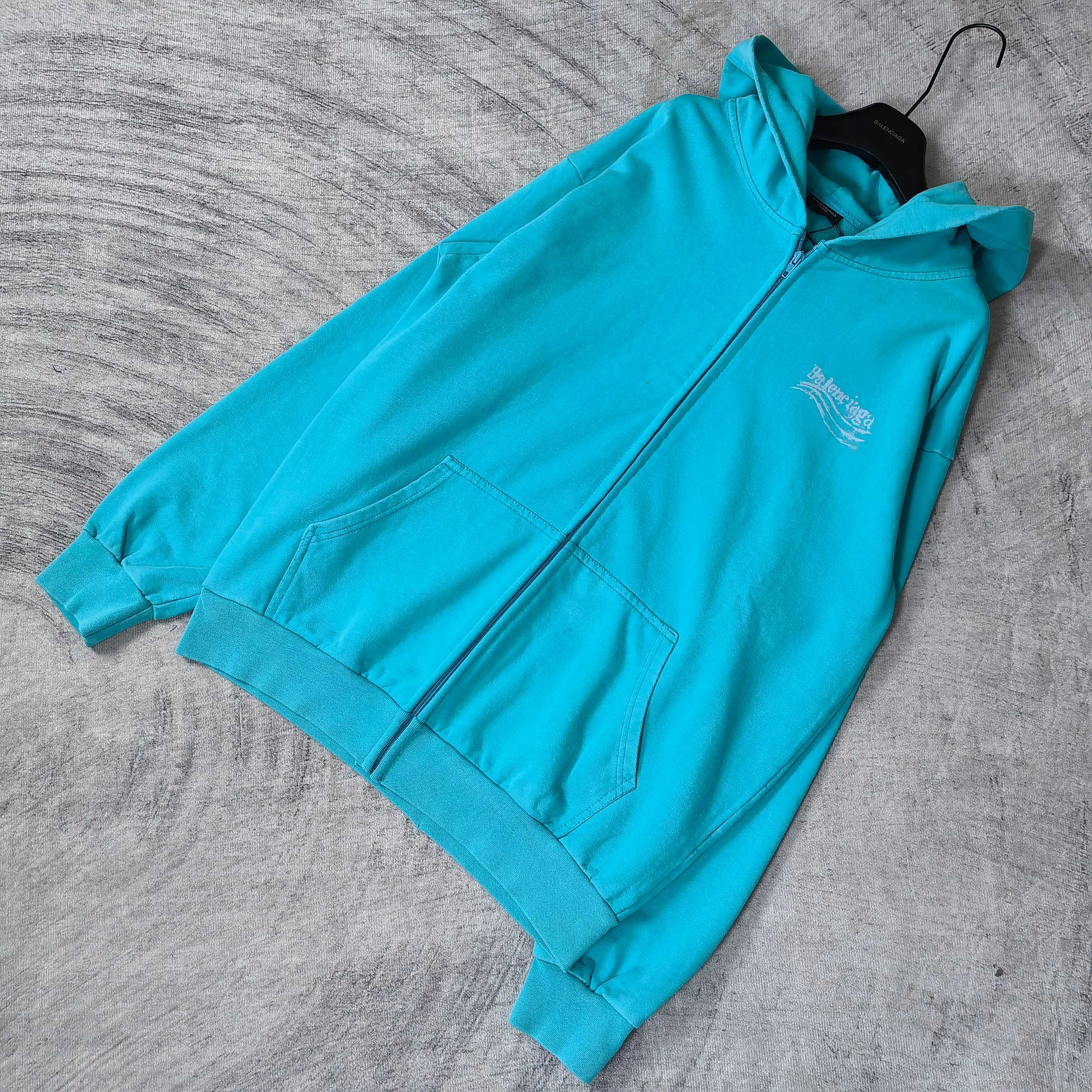 Turquoise zip-up hoodie with hood and front pocket, shown from side angle