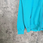 Turquoise hoodie sleeve and ribbed hem, front pocket opening visible