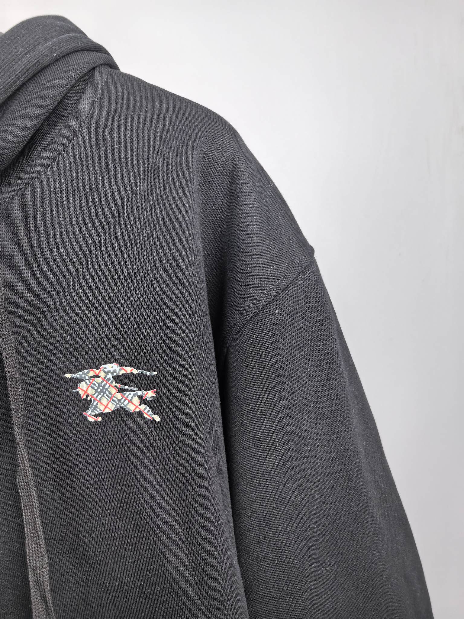 Black hoodie sleeve with small multicolor logo patch embroidery on the side.