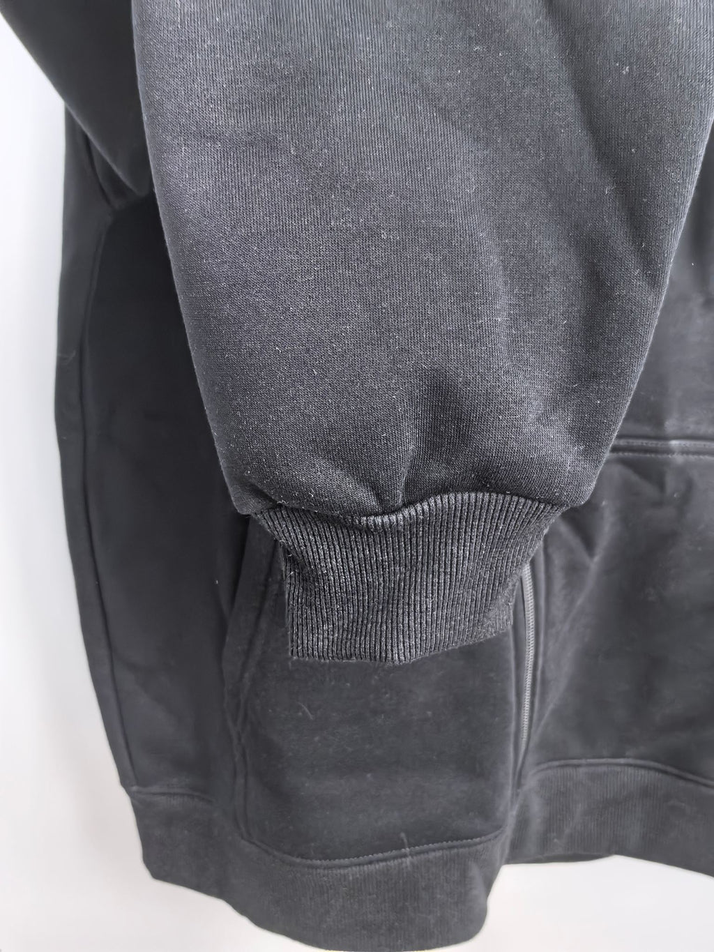 Black hoodie with ribbed knit cuff at the sleeve and textured fabric hem area.