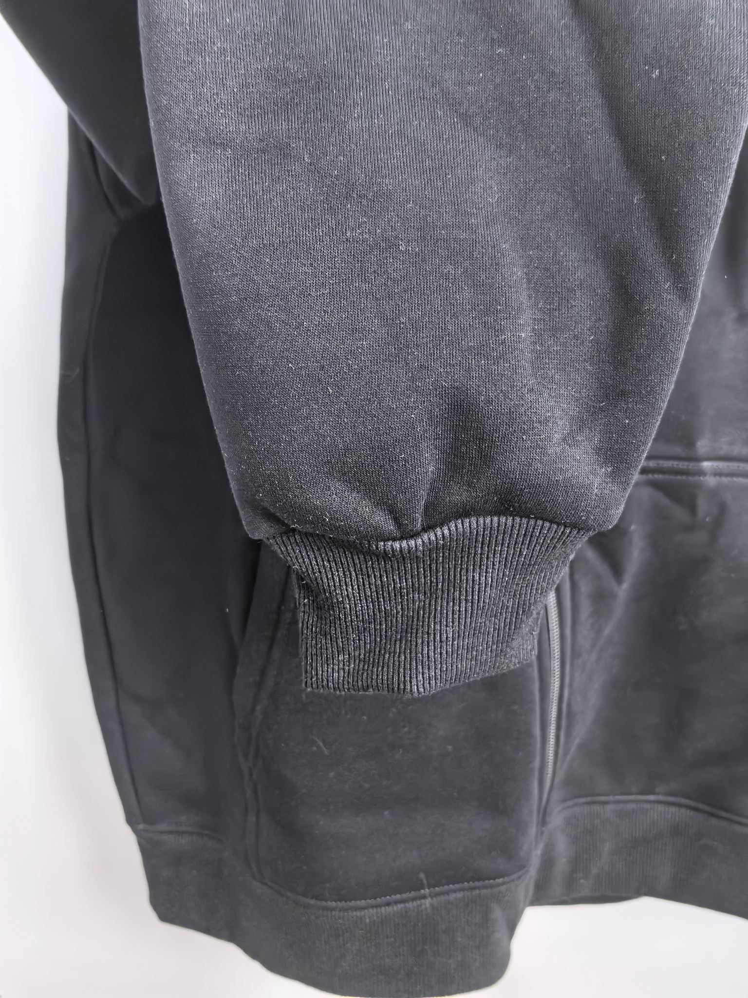Black hoodie with ribbed knit cuff at the sleeve and textured fabric hem area.