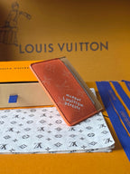 Small Louis Vuitton cardholder angled view in coral orange textured leather with monogram text.