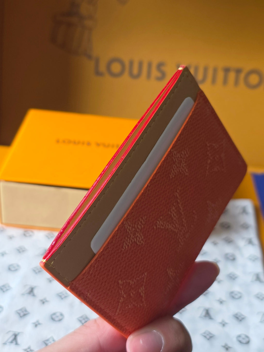 Small Louis Vuitton cardholder with coral orange exterior and beige interior panel, front edge.
